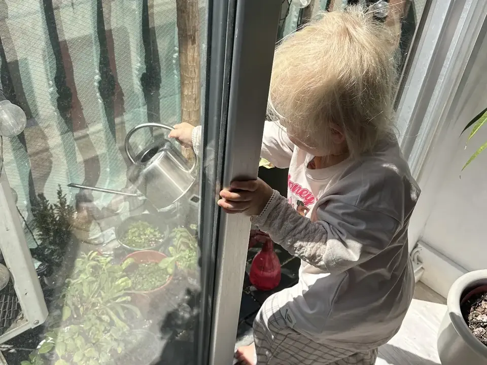 A child watering plants with a metal watering can